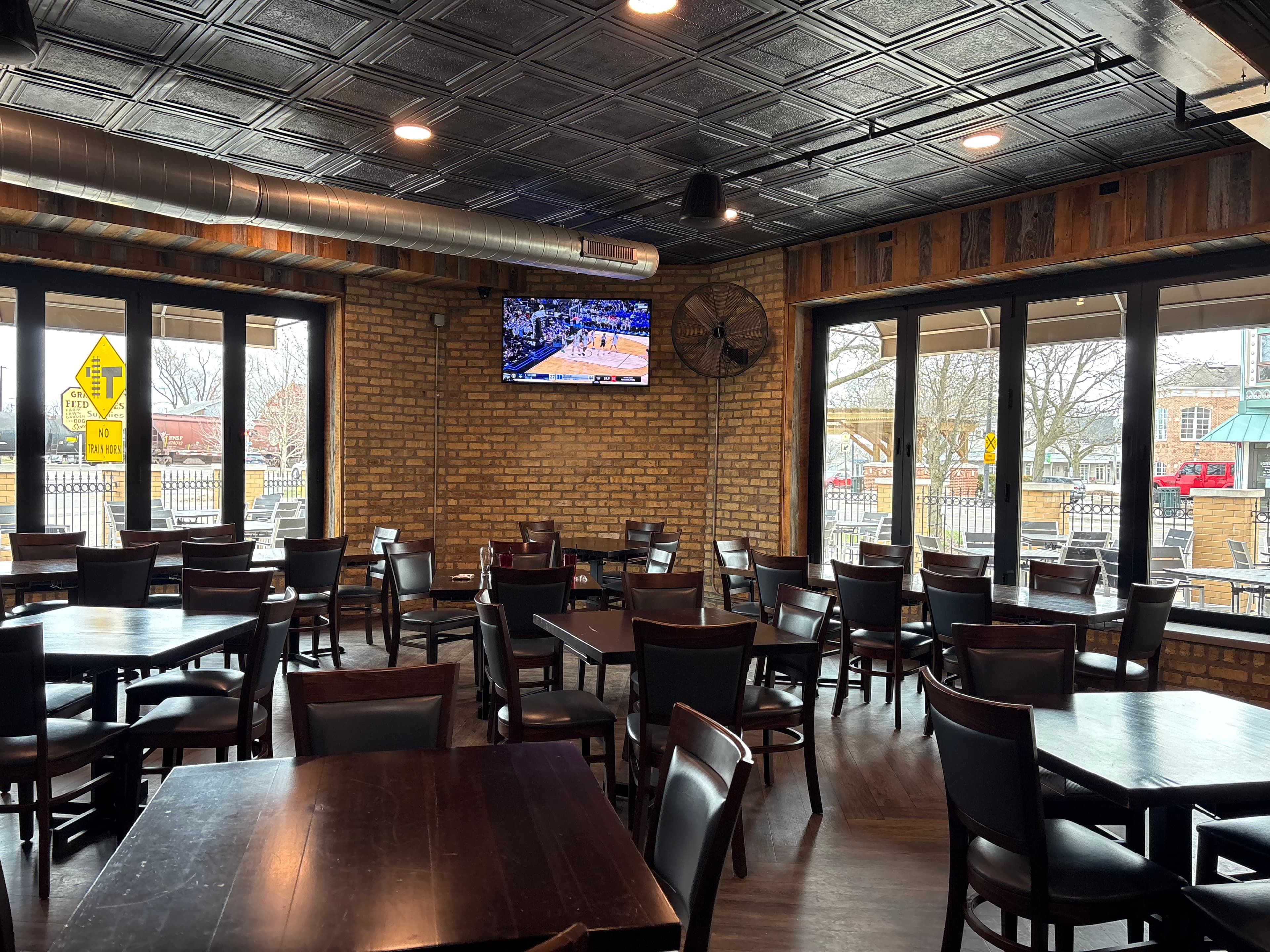 Rustic restaurant interior with dark wood tables, brick walls, and a television showing basketball.